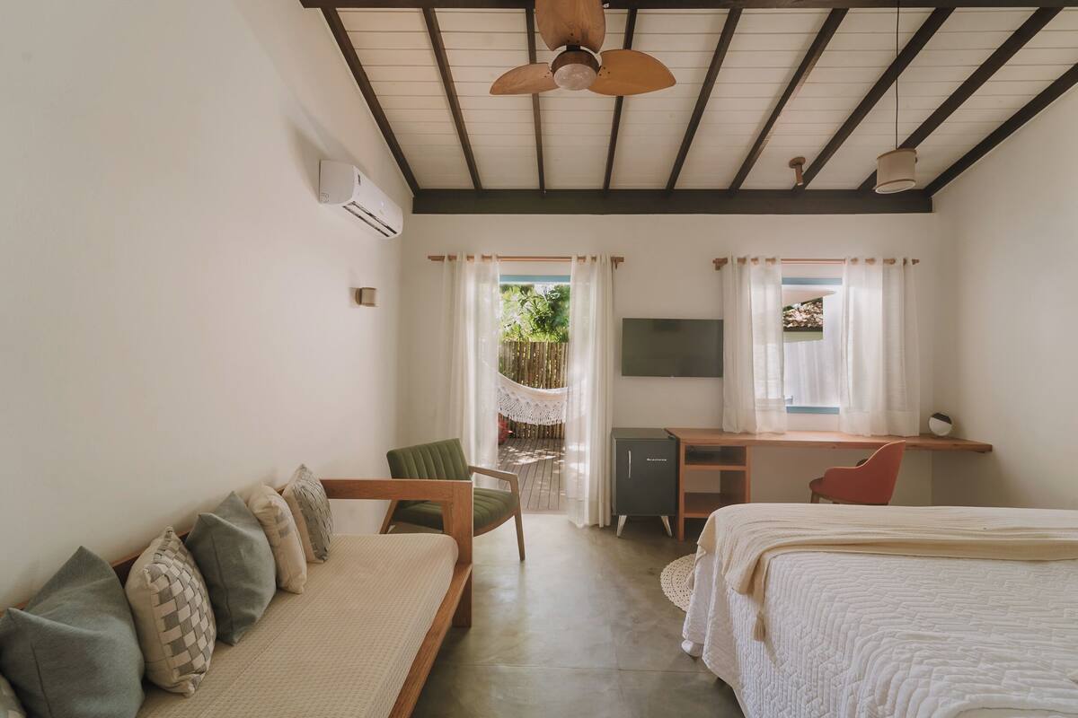 A bedroom with a bed, a desk, a chair, a sofa, and a ceiling fan.