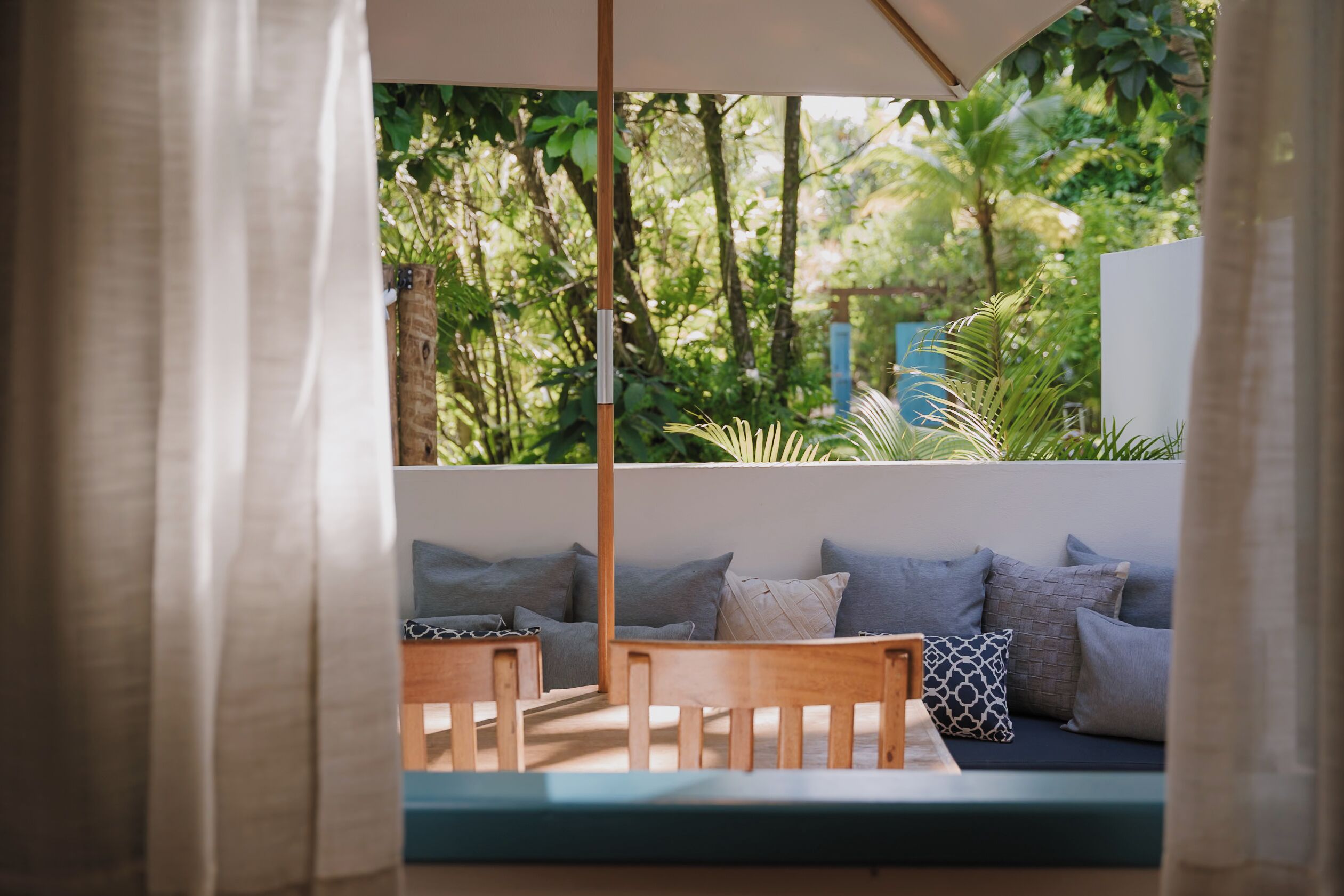 A cozy outdoor seating area with a wooden bench and cushions, surrounded by lush greenery.