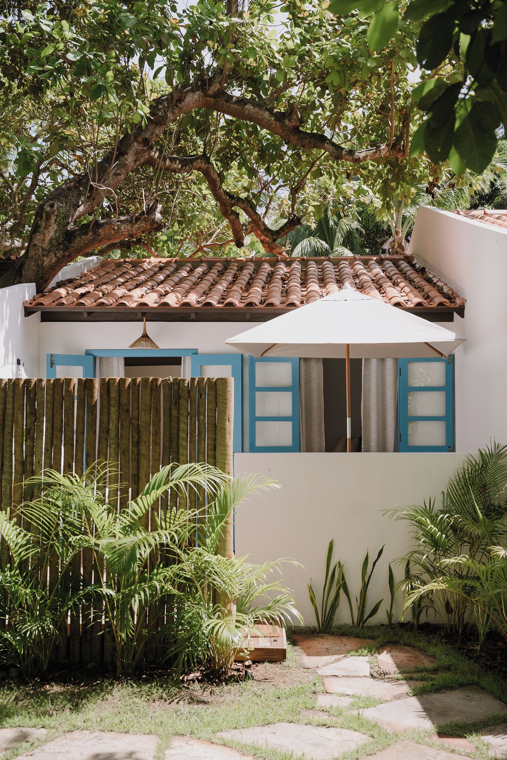 Una casa con techo de tejas, cerca de madera y jardín con diversas plantas.