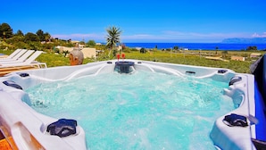 A hot tub with a clear view of the ocean and a grassy area with lounge chairs.