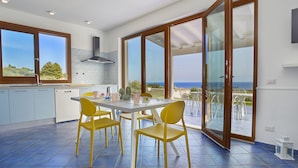 A modern kitchen with a dining area, large windows, and a view of the sea.