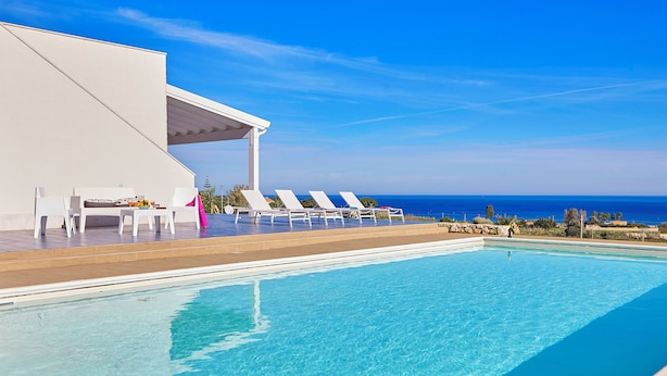 A poolside area with lounge chairs and a covered seating area overlooking the ocean.