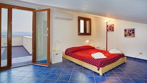 A bedroom with a bed, a window, a door, and a view of the sea.