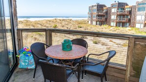 Een balkon met rieten stoelen en een tafel, met uitzicht op een strand en gebouwen.
