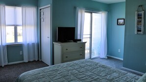 A bedroom with a bed, a dresser, a television on the dresser, and a window with curtains.
