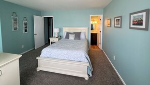 A bedroom with a bed, nightstand, and dresser. There is a door leading to a bathroom.