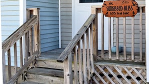 A wooden staircase leading to a porch with a sign reading "SUNKISSED BLISS 63 15 Teal Lane".