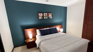 A bedroom with teal walls, a wooden headboard, a white bedspread, two pillows, a nightstand, and a bedside lamp.