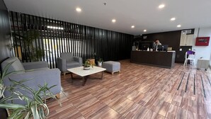 A modern reception area with a wooden floor, grey sofas, a coffee table, and a reception desk.