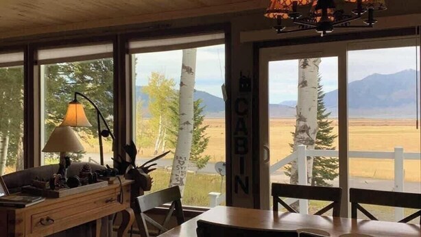 Una habitación con un escritorio de madera, una lámpara y vistas a las montañas a través de amplios ventanales.