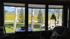 Una habitación con ventanas amplias, techo de madera y vistas a un paisaje de árboles y montañas.