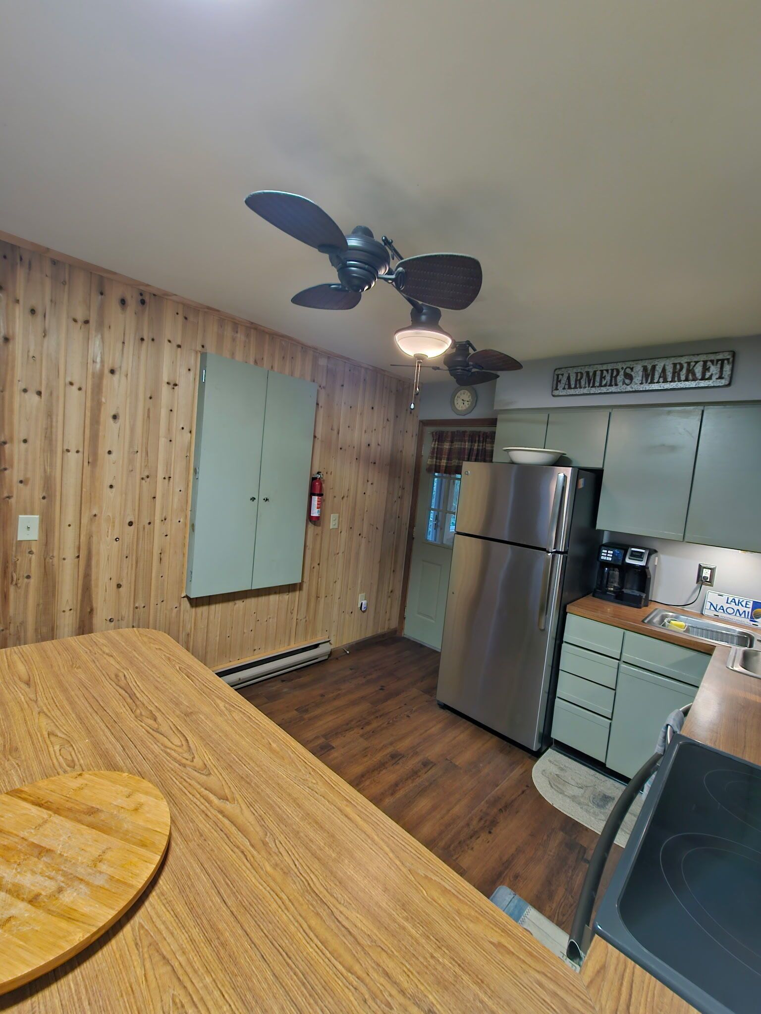 A kitchen with wooden walls, a stainless steel refrigerator, a coffee maker, and a sign that reads "FARMER'S MARKET".
