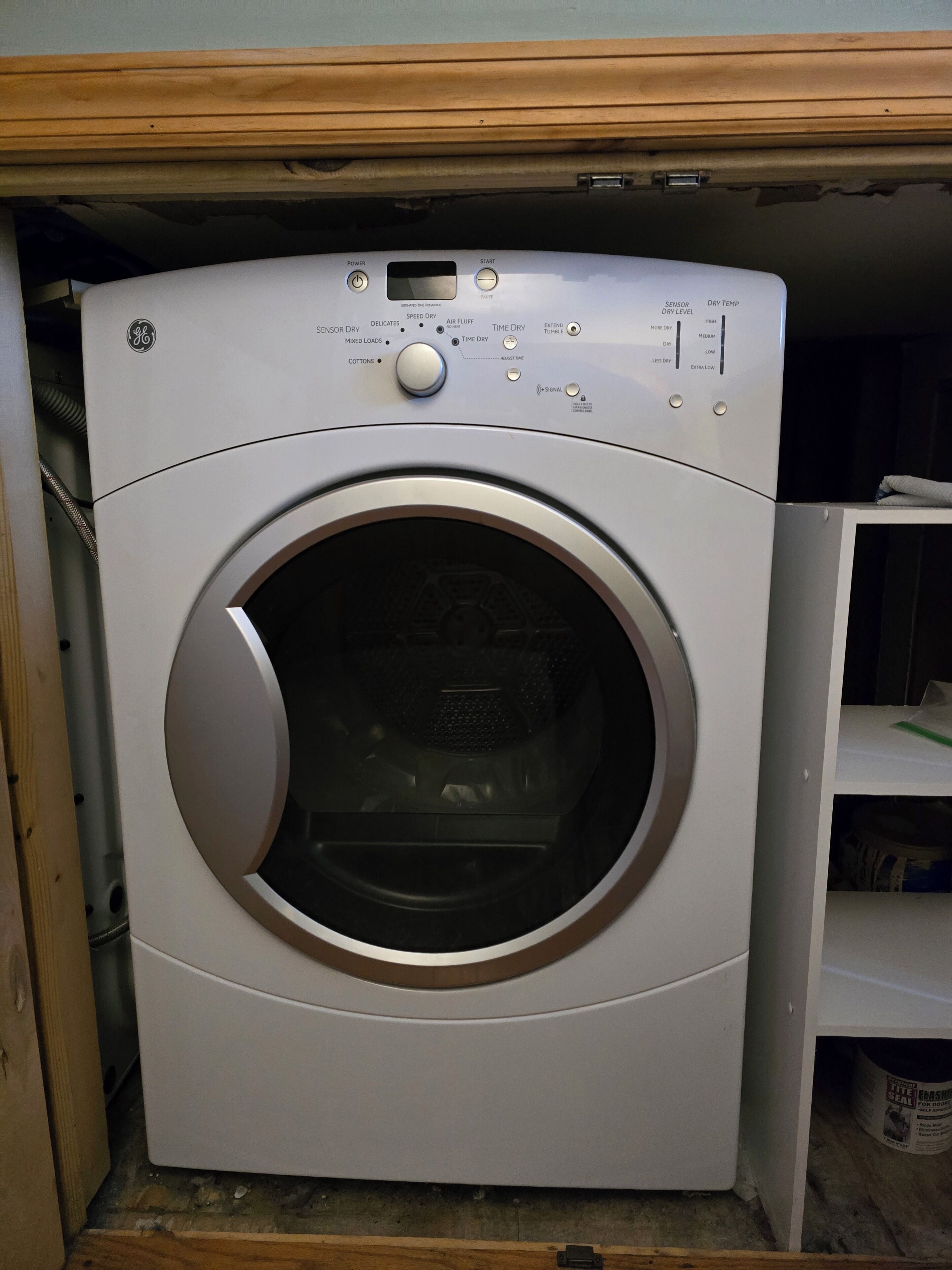 A front view of a GE front-loading washing machine with a control panel, installed in a wooden cabinet.