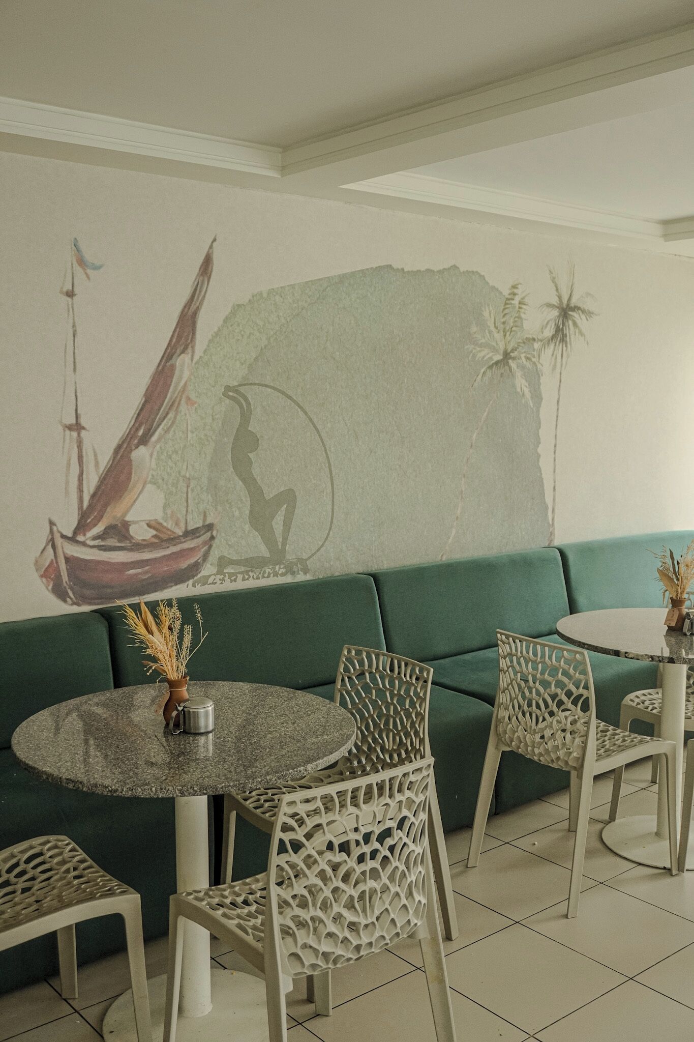 Un restaurant avec un canapé vert, une table ronde surmontée d’un pichet en métal et des chaises au motif ajouré.