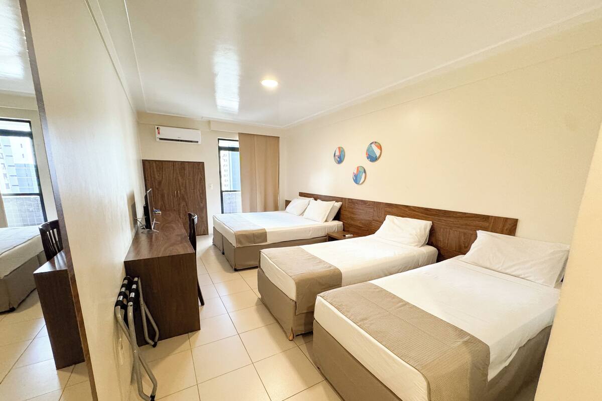 A hotel room with three beds, a desk, and a wheelchair.