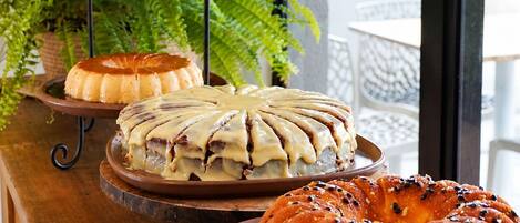 Una mesa buffet de madera con diversas opciones de panadería, incluyendo un pastel bundt con glaseado blanco, una tarta glaseada y un pastel bundt con semillas negras.