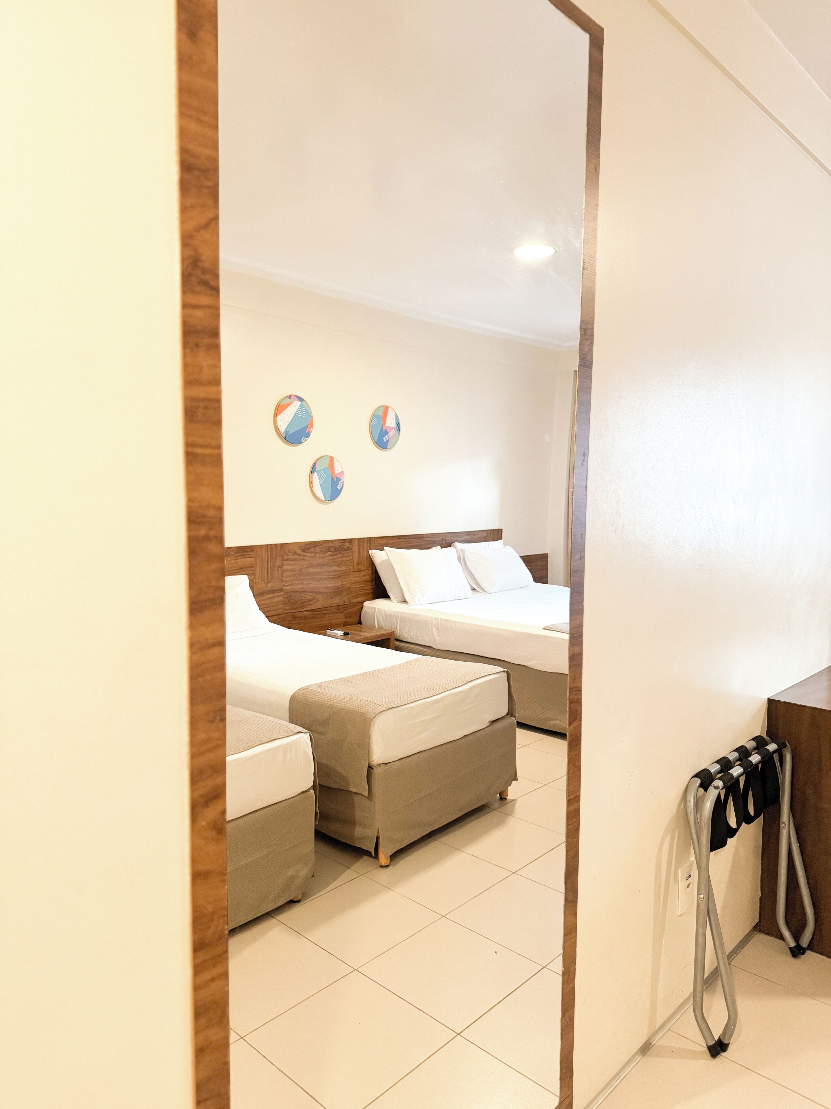 A hotel room with two beds, a wooden headboard, a small table, and a chair with a towel rack.