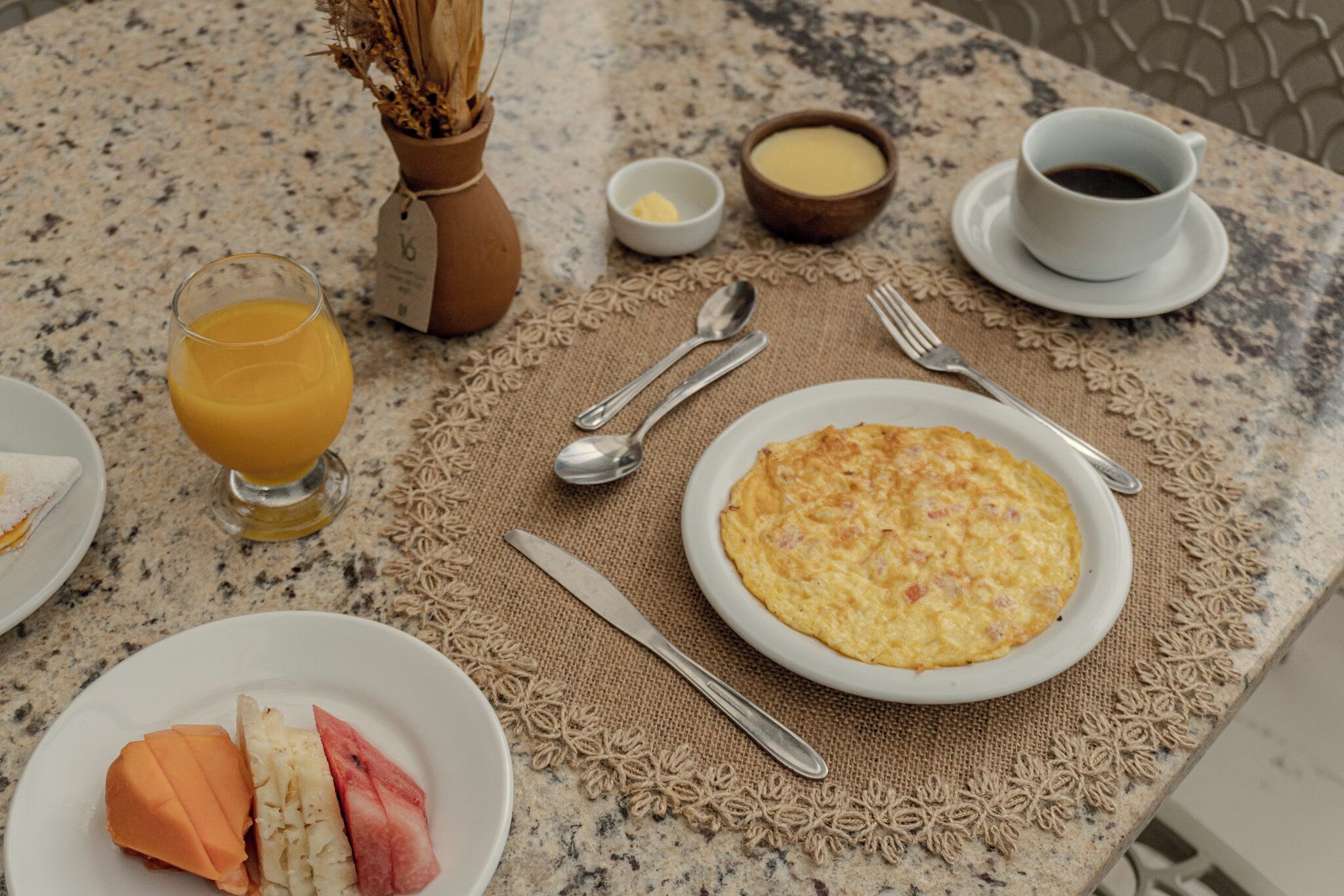 A breakfast table with a plate of eggs, a glass of orange juice, a bowl of butter, a cup of coffee, and a vase with dried flowers.