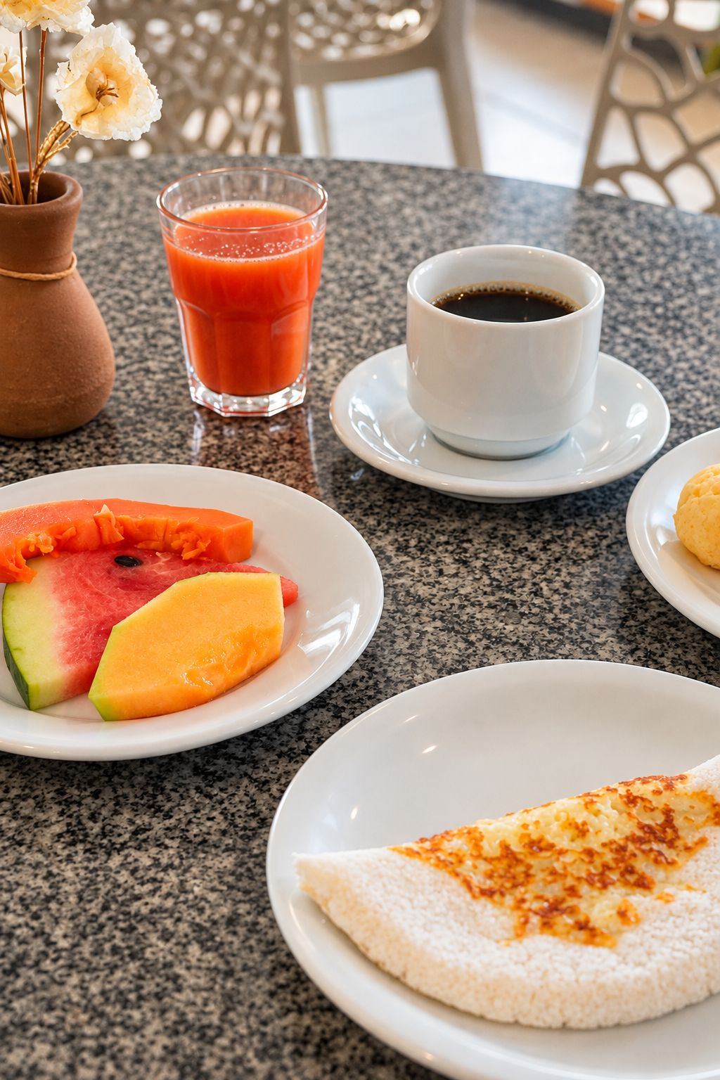 Ein Frühstückstisch mit einer Fruchtschale, einem Glas Saft, einer Kaffeetasse und einem Blätterteiggebäck.