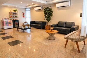 Un hall de hotel con recepción, asientos, una máquina de café y una planta en maceta.