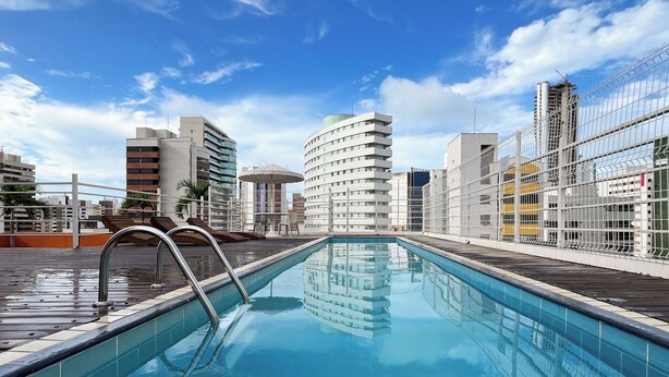 A rooftop pool with a metal ladder, surrounded by modern buildings and a clear sky. - D8 Hotel Express (Fortaleza)