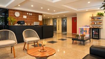 Un hall de hotel con una recepción, dos sillones, una mesa de centro y un refrigerador.