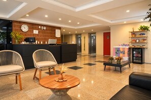 A hotel lobby with a reception desk, two chairs, a coffee table, and a refrigerator. - D8 Hotel Express (Fortaleza)