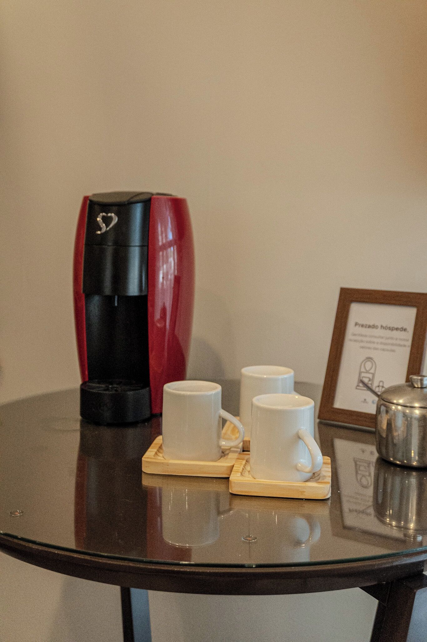 A coffee maker, two white cups, and a framed sign on a table.
