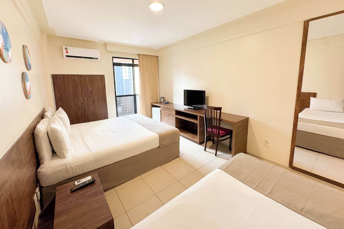 A hotel room with a bed, a desk, a chair, a TV, and a large mirror.