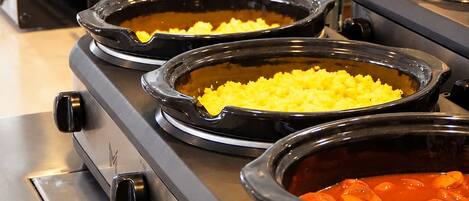 A buffet setup with various food items in black serving dishes on a stainless steel stove.