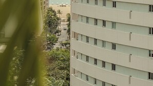 A high-rise building with multiple floors, a view of the ocean, and a street with parked cars and greenery. - D8 Hotel Express (Fortaleza)