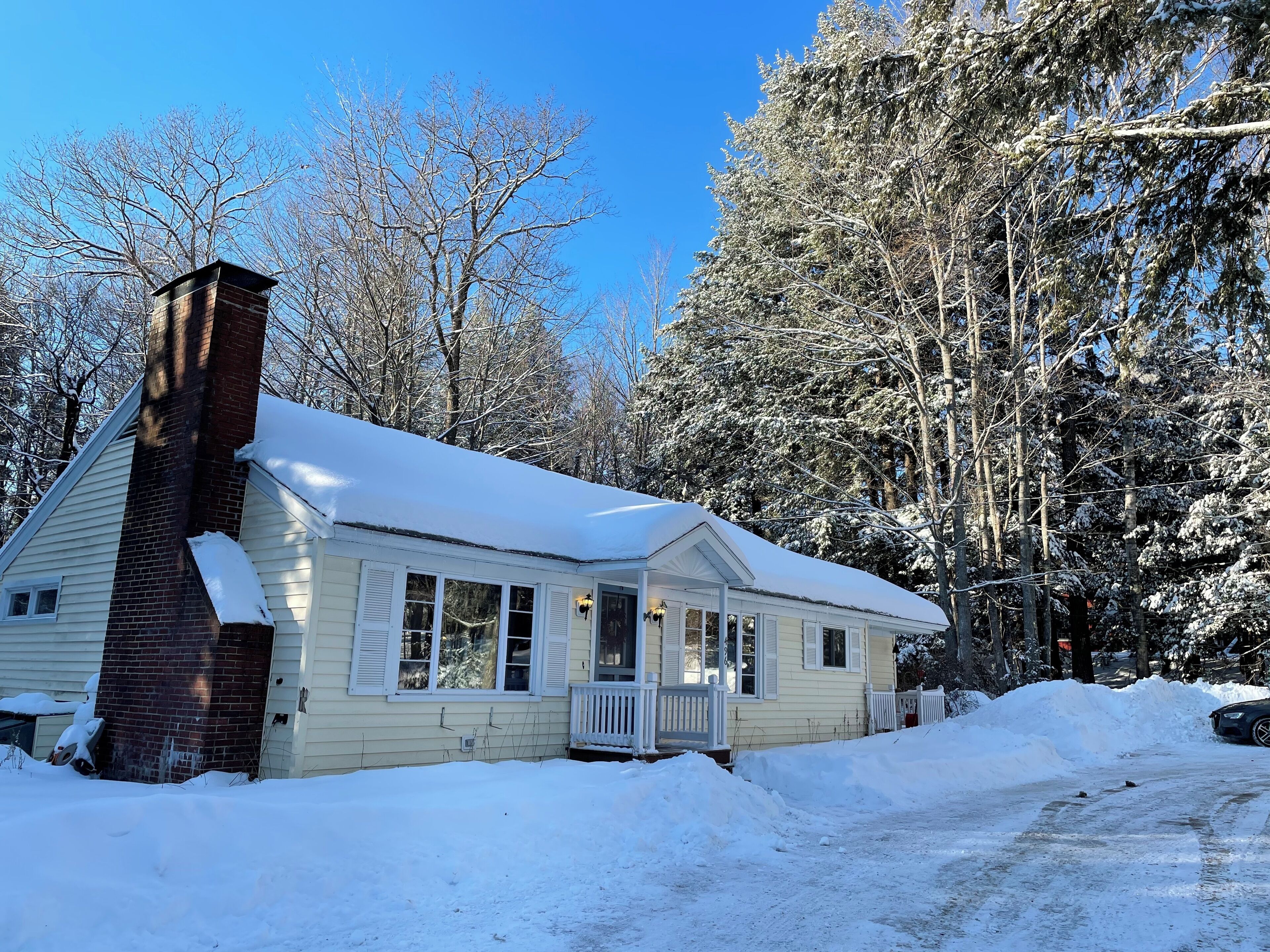 A single-story house with a brick chimney, a porch, and a snow-covered roof.