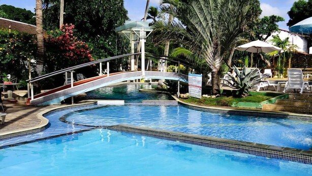 Une piscine avec un pont, entourée de palmiers et de chaises longues.