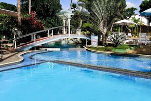 Una piscina amb un pont, rodejada de palmeres i gandules.
