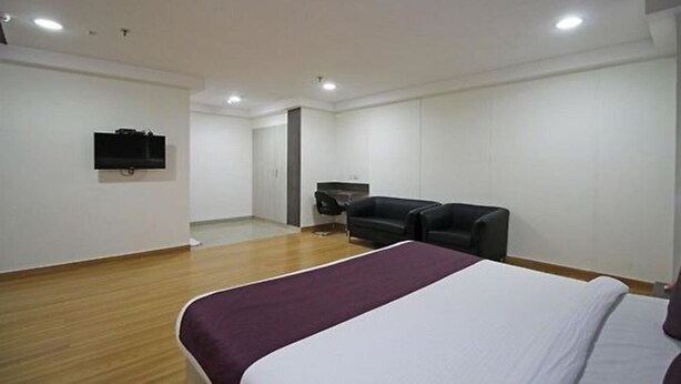 A hotel room with a bed, a TV mounted on the wall, a black leather chair, and a desk with a chair. - OYO Rooms Noida Sector 62 (Noida)