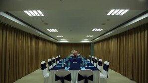 A conference room with a long table, white chairs with dark sashes, and a blue tablecloth. - OYO Rooms Noida Sector 62 (Noida)