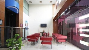 A conference room with red chairs arranged in rows, a large screen on the wall, and a potted plant in the corner. - OYO Rooms Noida Sector 62 (Noida)