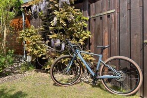 Ein Fahrrad vor einem Holzzaun mit einem Garten und einem Gebäude im Hintergrund.