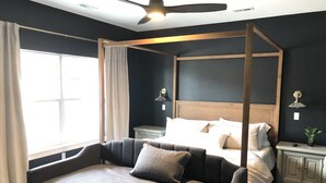 Un dormitorio moderno con cama con dosel, una mesita de noche con lámpara y un atril con una planta.