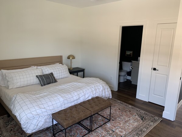 A bedroom with a bed, bedside table, lamp, bench, and a view into the bathroom.
