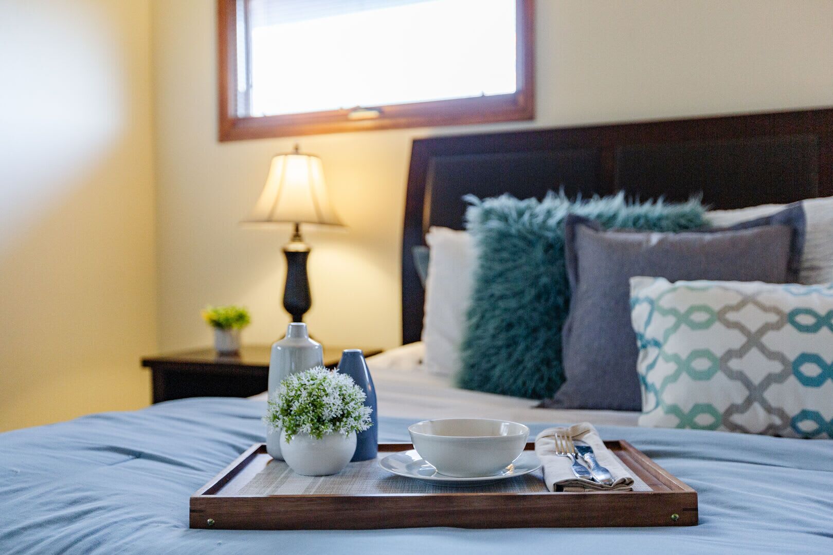 A neatly made bed with a tray of breakfast items, a lamp, and a view of the room's headboard and pillows.