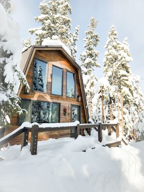 Eine Holzhütte mit geneigtem Dach, großen Fenstern und einer Holzterrasse.