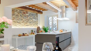 Une cuisine moderne avec un mur de pierres apparentes derrière l’évier, des poutres en bois et une grande fenêtre.