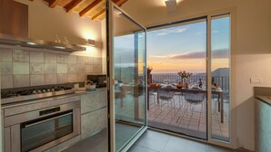 Une cuisine moderne dotée d’un grand îlot central, un coin repas offrant une vue sur le coucher de soleil et un balcon avec une table préparée pour deux personnes.