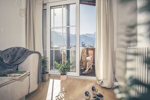 Een gezellige woonkamer met een bank, een bijzettafeltje, een potplant en een paar schoenen op de vloer.