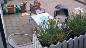 Une terrasse extérieure avec une table, des chaises, des plantes en pot et une clôture blanche en bois.