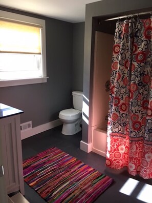 A bathroom with a toilet, a shower curtain with a floral pattern, and a colorful striped rug.