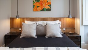 A hotel room with a bed, two bedside tables, a wooden headboard, a painting of a flower, and a wall-mounted lamp.