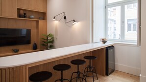 A modern kitchen with wooden cabinets, a built-in TV, bar stools, and a window with a view of buildings.