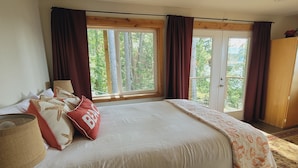 Une chambre avec un grand lit, une fenêtre avec des rideaux, un plafond en bois et une vue sur la verdure.